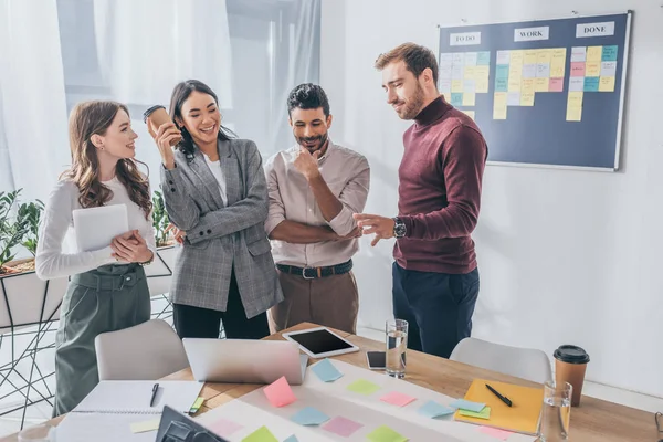 Multicultural businesswomen and businessmen near table with gadgets in office — Stock Photo