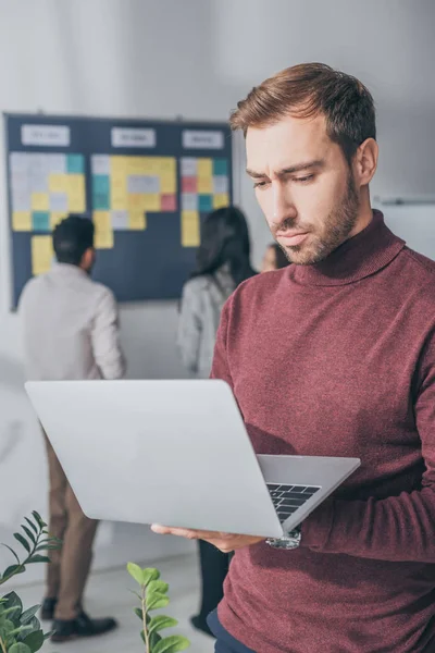 Foyer sélectif de bel homme d'affaires en utilisant un ordinateur portable dans le bureau — Photo de stock