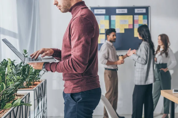 Cropped view of businessman using laptop near multicultural coworkers — Stock Photo