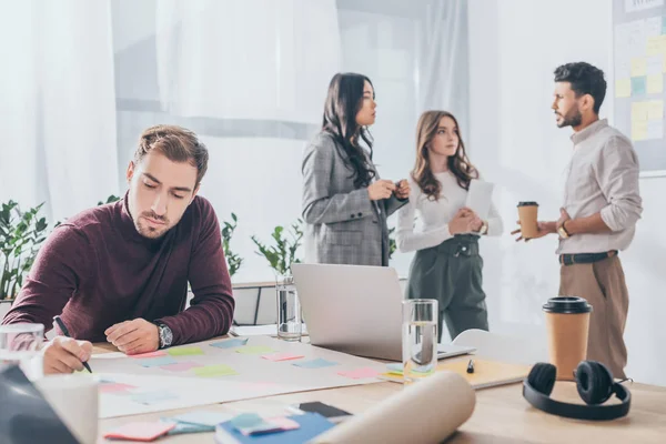 Selective focus of businessman writing on sticky note near coworkers — Stock Photo