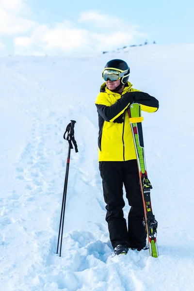 Deportista feliz en el casco de pie cerca de bastones de esquí en la nieve - foto de stock