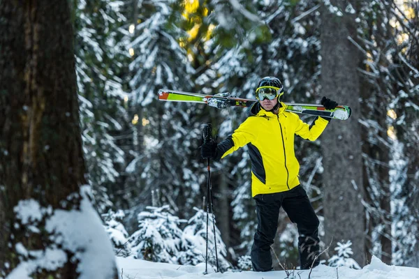 Enfoque selectivo de esquiador en gafas con bastones de esquí y esquís de pie cerca de abetos - foto de stock