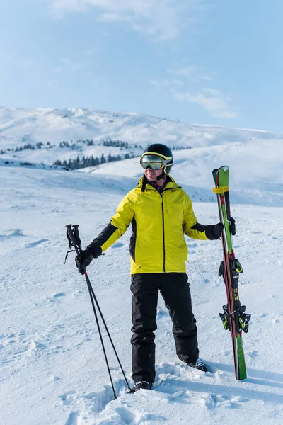 Sciatore in casco in piedi con bastoni su neve bianca in montagna — Foto stock