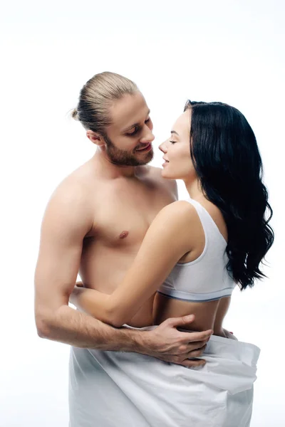 Сексуальна усміхнена молода пара обіймається білими простирадлами, ізольована на білому — стокове фото