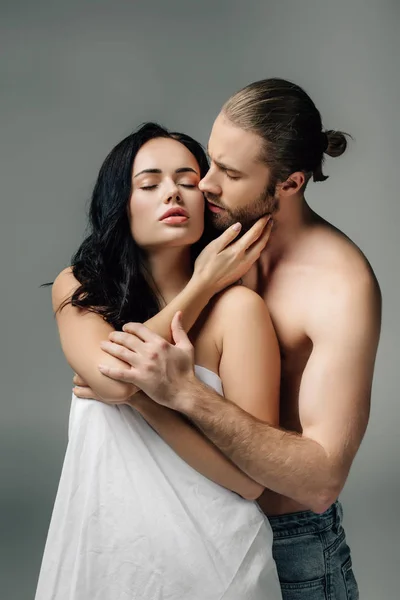 Seductive nude couple hugging in sheets, isolated on grey — Stock Photo