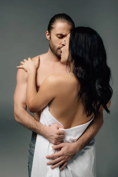 Apasionada pareja desnuda abrazándose en sábanas, aislada en gris - foto de stock