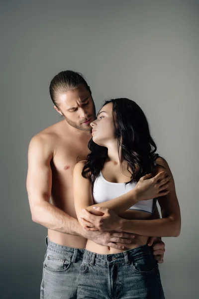 Hemdloser Mann umarmt attraktive Freundin isoliert auf grau — Stockfoto