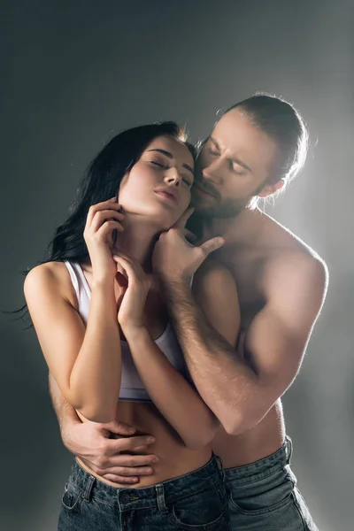 Hermosa sexy joven pareja abrazándose en gris con luz de fondo - foto de stock