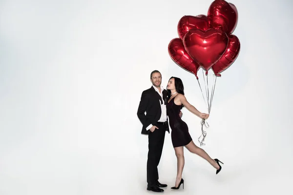 Beautiful positive couple holding red heart shaped balloons on valentines day on white — Stock Photo