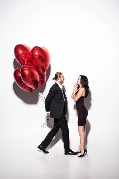 Alegre pareja sosteniendo rojo corazón en forma de globos en San Valentín día en blanco - foto de stock