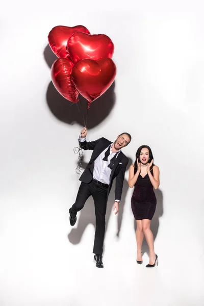Excited couple holding red heart shaped balloons on valentines day on white — Stock Photo