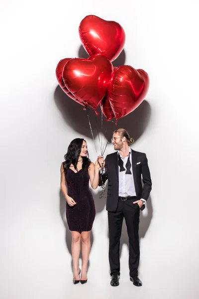 Smiling couple holding red heart shaped balloons on valentines day on white — Stock Photo