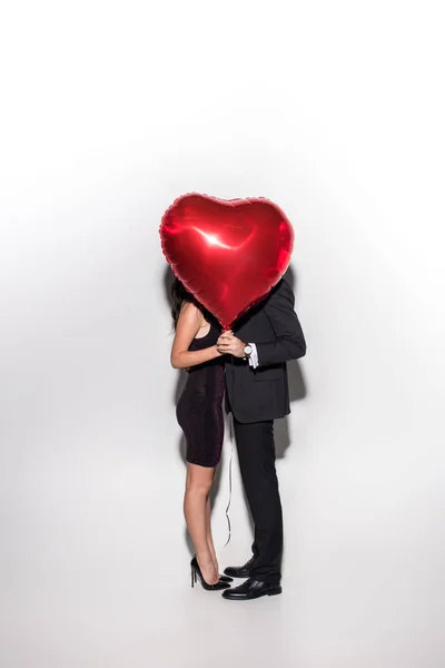 Pareja sosteniendo el globo rojo en forma de corazón delante de la cara en el día de San Valentín en blanco - foto de stock