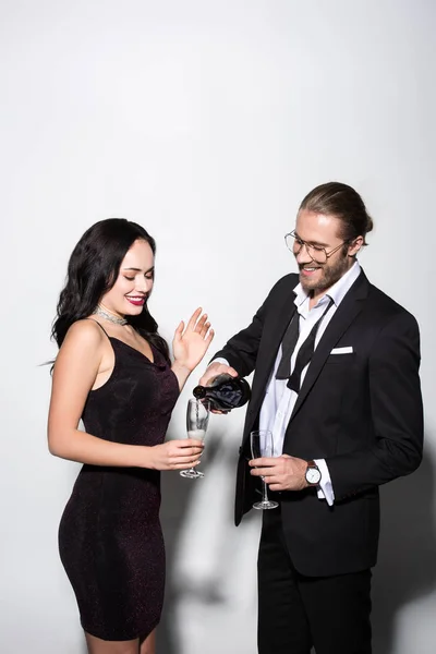 Beau couple heureux versant champagne de bouteille dans des verres pour la Saint-Valentin sur blanc — Photo de stock