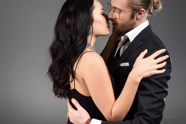 Beautiful sensual couple in black suit and dress kissing isolated on grey — Stock Photo