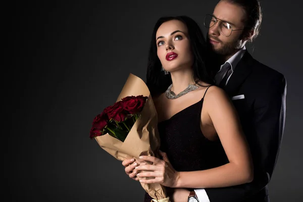 Красива молода пара тримає букет червоних троянд в день валентинки, ізольована на сірому — стокове фото