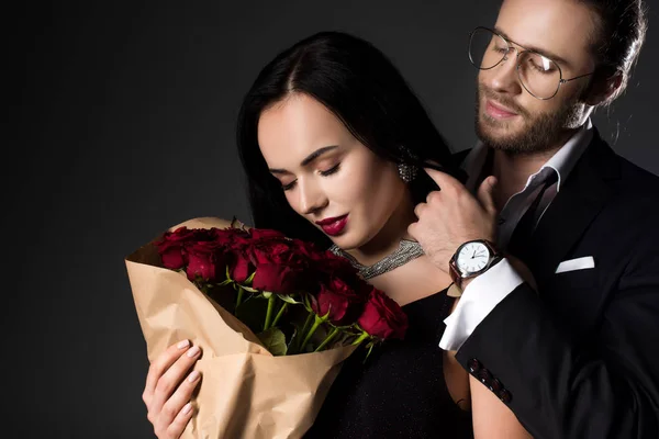 Beautiful couple holding bouquet of red roses on valentines day, isolated on grey — Stock Photo