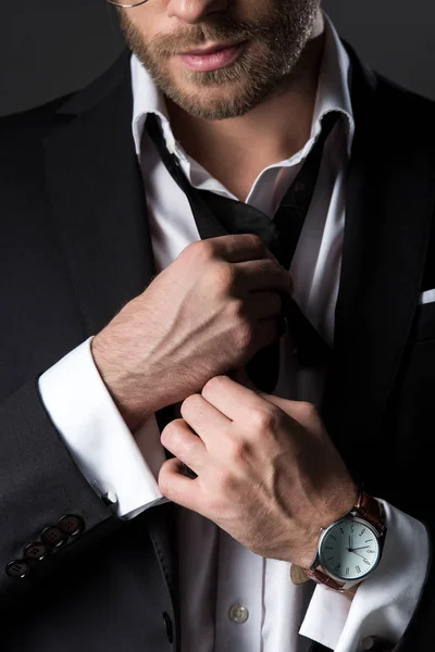 Vista recortada del hombre en traje ajustando corbata aislado en gris - foto de stock