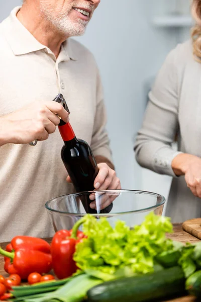 Cropped view of woman cooking and man opening bottle with wine — Stock Photo