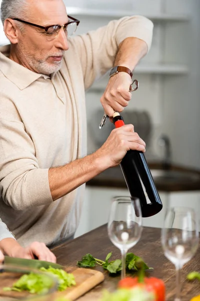 Messa a fuoco selettiva dell'uomo aprendo bottiglia con vino e donna taglio lattuga su sfondo — Foto stock