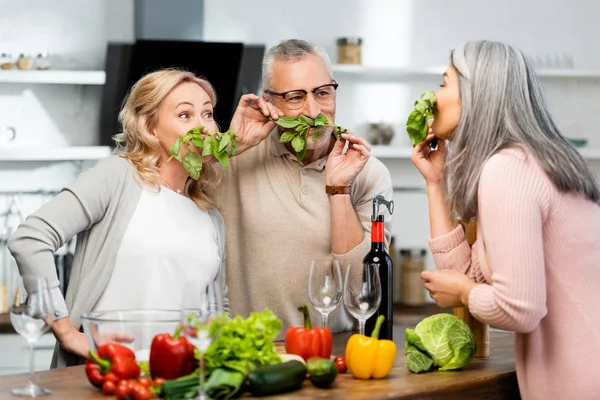 Trois amis souriants sentant le basilic bio et vert dans la cuisine — Photo de stock