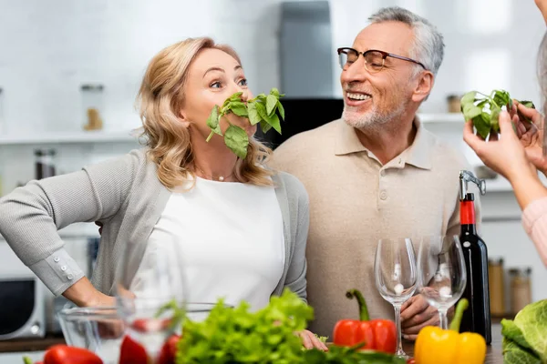 Mulher atraente com manjericão olhando para seus amigos sorridentes na cozinha — Fotografia de Stock