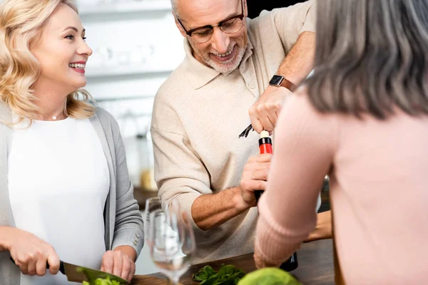Селективное внимание мужчины, открывающего бутылку с вином и женщиной, режущей салат — стоковое фото