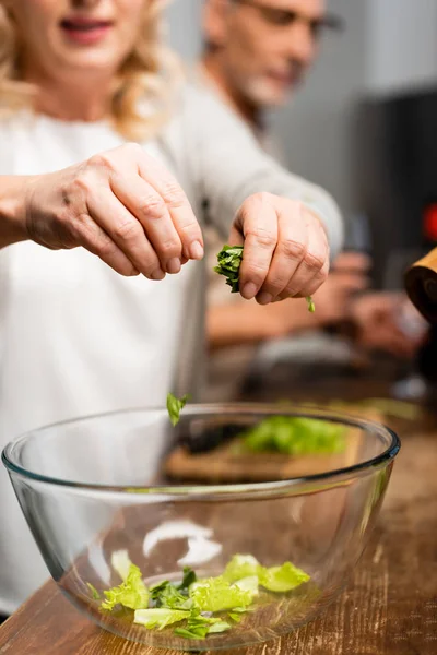 Vista ritagliata della donna che aggiunge lattuga alla ciotola in cucina — Foto stock