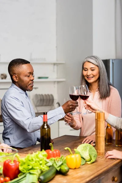 Vista ritagliata di sorridenti amici multiculturali clinking con bicchieri di vino — Foto stock