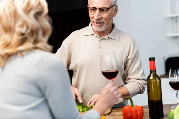 Cropped view of woman talking with smiling friend and he cutting lettuce — Stock Photo