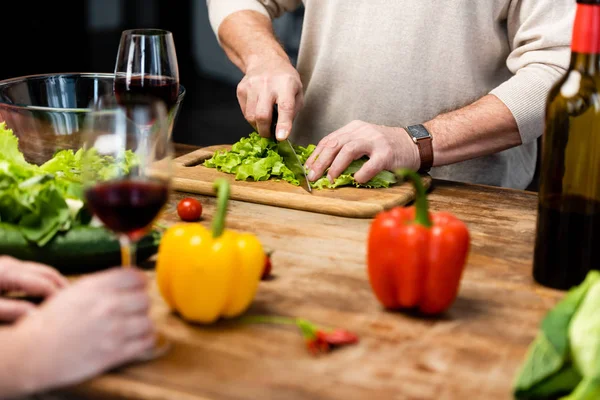 Cropped view of woman holding wine glass and man cutting lettuce — Stock Photo