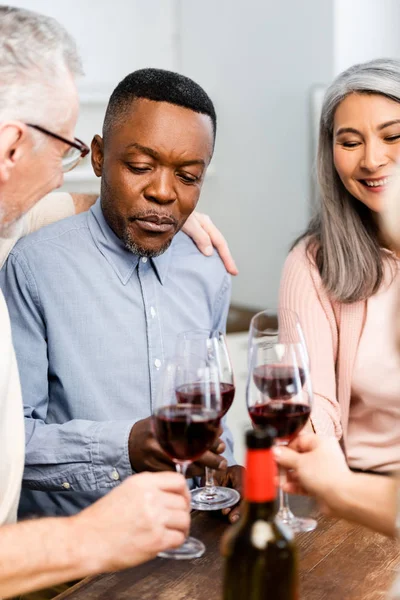 Recortado vista de sonrientes amigos multiculturales tintineo con copas de vino en la cocina - foto de stock