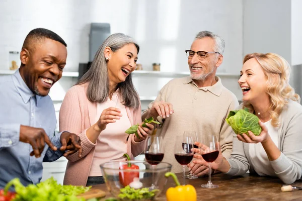 Усміхнені багатокультурні друзі розмовляють і стоять біля столу на кухні — стокове фото