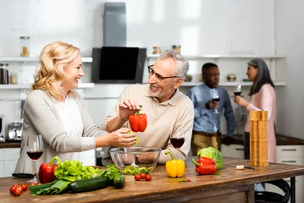 Selektiver Fokus der Frau mit Salat und lächelnder Mann mit Paprika, multikulturelle Freunde reden über Hintergrund — Stockfoto