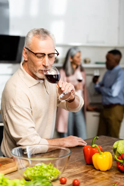 Selective focus of man drinking wine and multicultural friends talking on background — Stock Photo