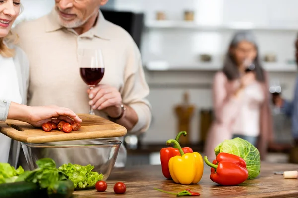Обрізаний вид усміхненої жінки, що додає нарізані вишневі помідори до миски і чоловік тримає келих для вина — стокове фото