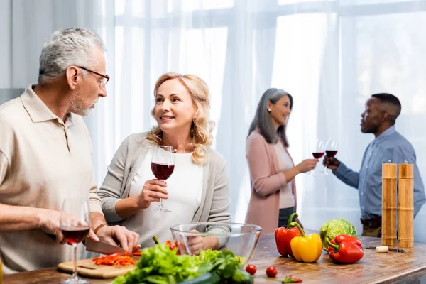 Selective focus of man cutting bell pepper and talking with woman, multicultural friends talking on background — Stock Photo