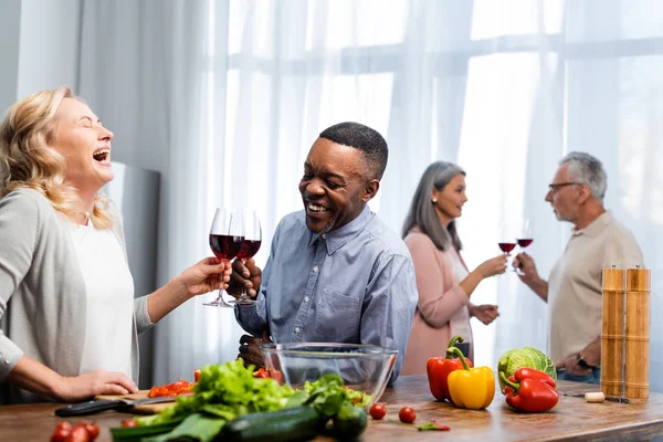 Focalizzazione selettiva di donna sorridente e uomo afro-americano clinking, amici multiculturali che parlano sullo sfondo — Foto stock