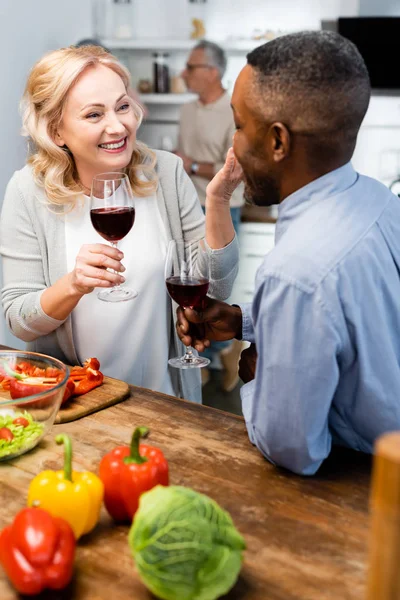 Mulher sorridente e homem americano africano falando e segurando copos de vinho — Fotografia de Stock