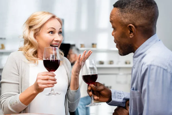 Mulher sorridente e homem americano africano falando e segurando copos de vinho — Fotografia de Stock