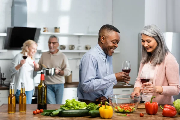Selective focus of smiling multicultural friends talking and holding wine glasses — Stock Photo