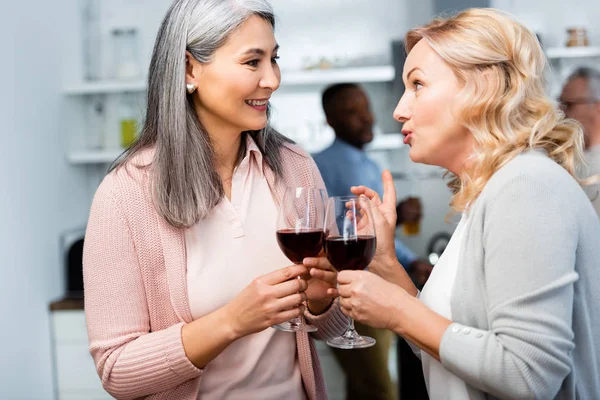 Smiling woman talking with asian friend and holding wine glass — Stock Photo