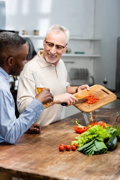 Африканский американец держит пиво и его друг добавляет помидоры черри в салат — стоковое фото