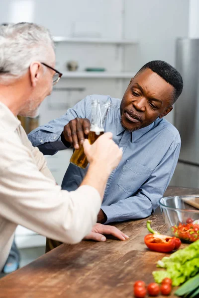 Вибірковий фокус афроамериканського чоловіка, що чіпляється зі своїм другом на кухні — стокове фото