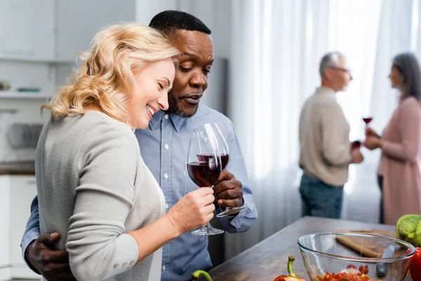 Selective focus of african american man hugging and clinking with smiling friend in kitchen — Stock Photo