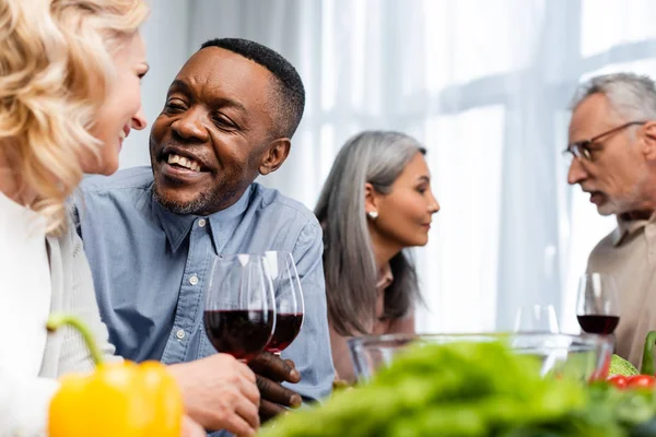 Focus selettivo di amici multiculturali che parlano e tengono bicchieri di vino — Foto stock