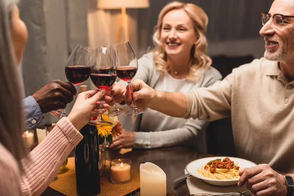 Enfoque selectivo de sonreír amigos multiculturales tintineo durante la cena - foto de stock