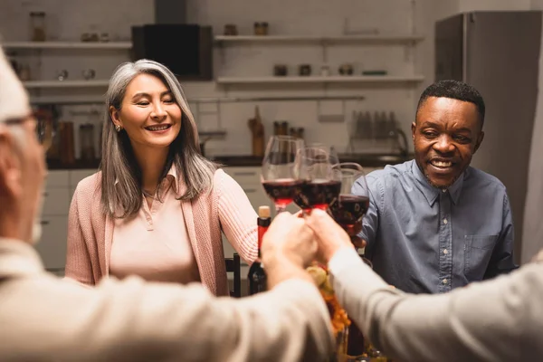 Foco seletivo de amigos multiculturais sorridentes clinking durante o jantar — Fotografia de Stock