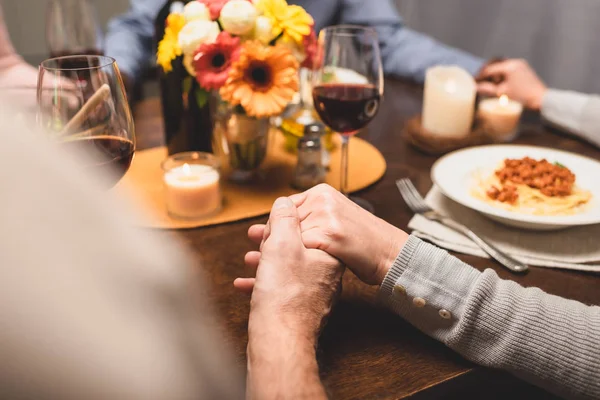 Vista cortada do homem segurando a mão de amigo e orando durante o jantar — Fotografia de Stock