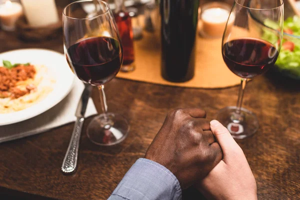 Vista recortada del hombre afroamericano cogido de la mano de un amigo y rezando durante la cena - foto de stock